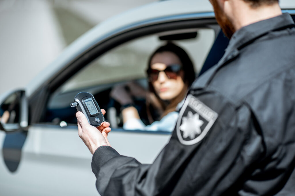 Policeman holding device for checking alcohol intoxication or dui while standing near the stopped car with woman driver