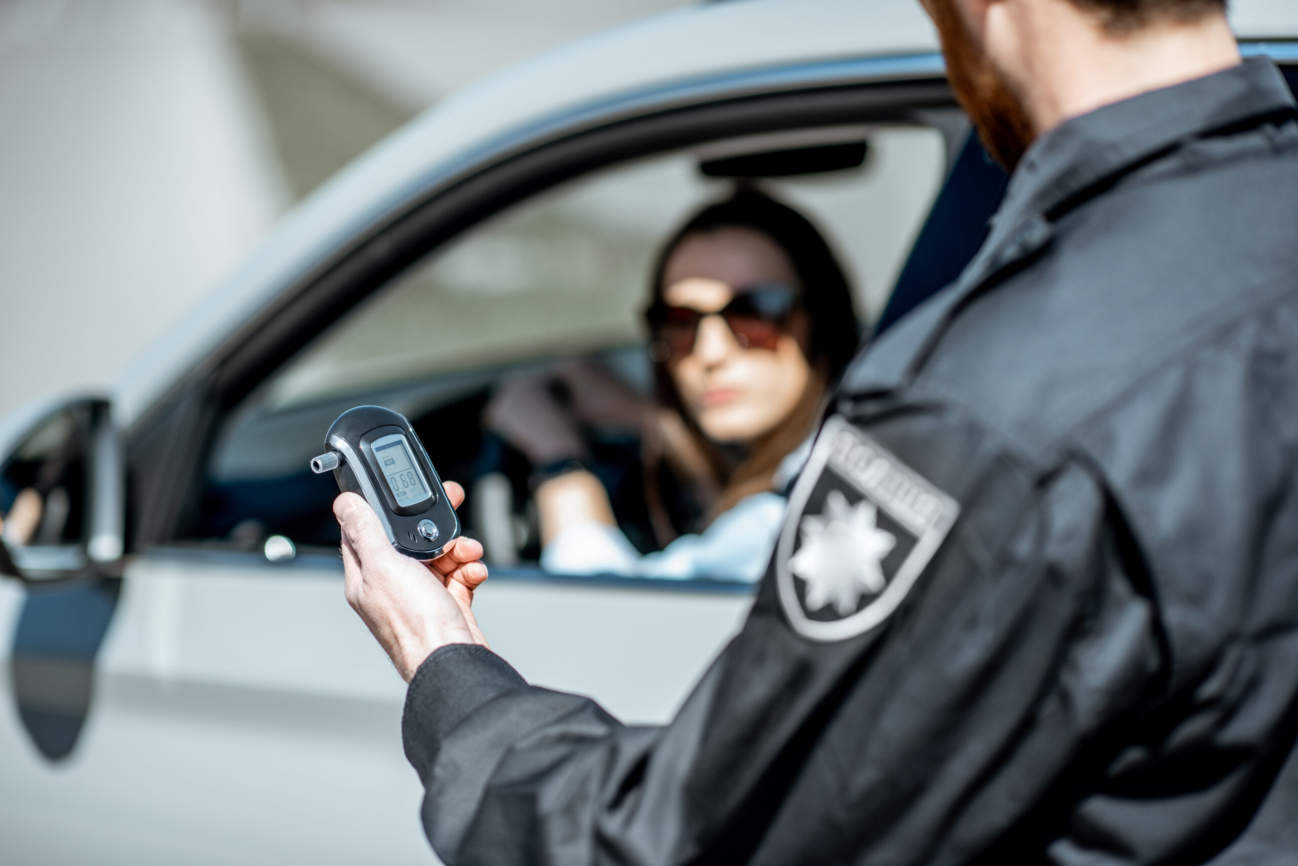 Policeman holding device for checking alcohol intoxication or dui while standing near the stopped car with woman driver